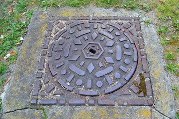 Decorative metal forged sewer hatch cover in green grass, top view close up