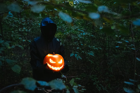 A black man in hands holds a Helluin pumpkin in a dark forest