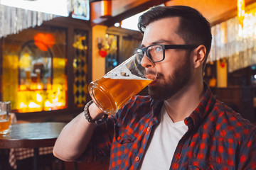 A young guy in glasses drinks beer in a close-up bar