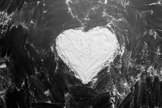 White flour heart shape in middle on black background texture photo, lines drawn with finger on flour, abstract. monochrome, black and white. top view.