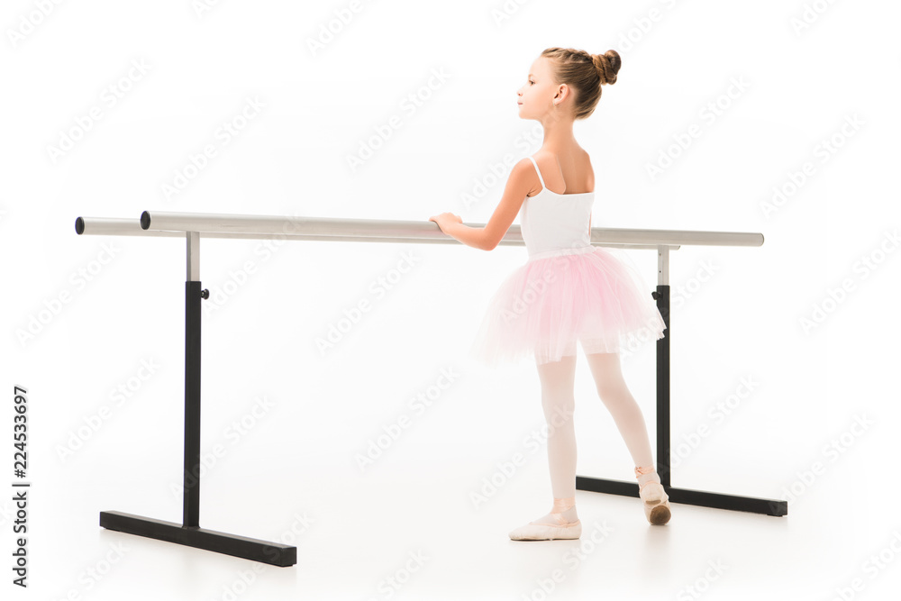 Wall mural rear view of beautiful little ballerina in tutu exercising at ballet barre stand isolated on white background