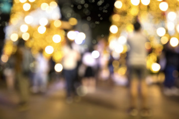 Blurry background image of defocused outdoor Christmas decorations with colorful lights and crowd of people in busy city street at night