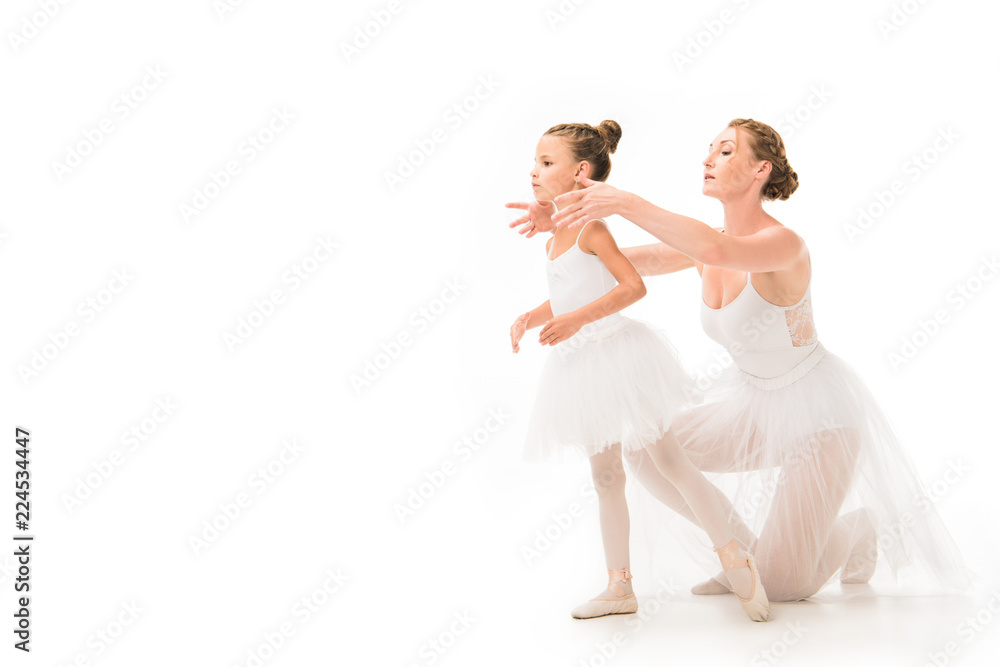 Wall mural adult female trainer in tutu helping little ballerina exercising isolated on white background