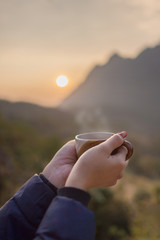 hands and coffee cup on the morning with sunrise background