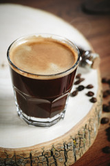 A cup of coffee with small white ceramic dish full of coffee beans on wooden background.