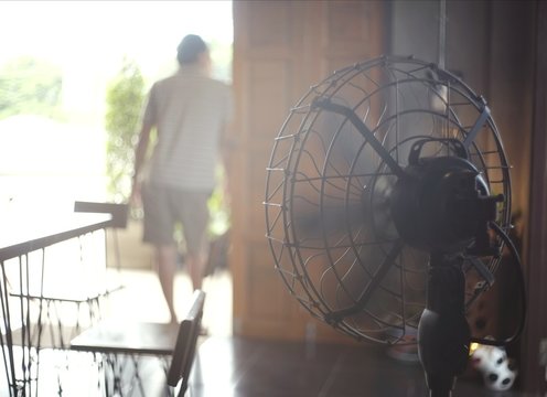 The black fan is working to blow the wind to relax the heat of the man standing at the door.