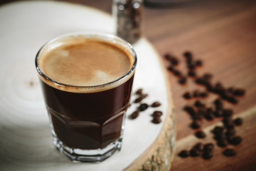 A cup of coffee with small white ceramic dish full of coffee beans on wooden background.