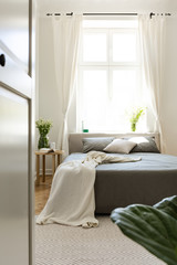 Vertical view into a sunny harmony bedroom interior with a bed placed against a bright big window...