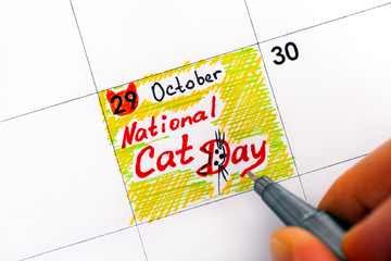 Woman fingers with pen writing reminder National Cat Day in calendar.