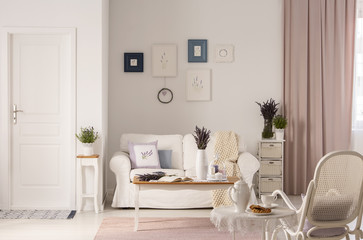 Flowers on table in front of white sofa in pink living room interior with door and armchair. Real...