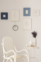 Flowers on table next to armchair in white living room interior with posters on the wall. Real photo