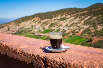 Glass with black coffee on the background of the Atlas mountain range covered with bright green...