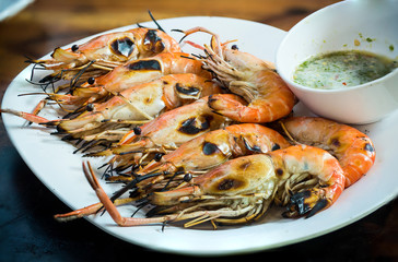 Close up roasted prawn on white plate with spicy sour sauce at seafood market, delicious thai street food 