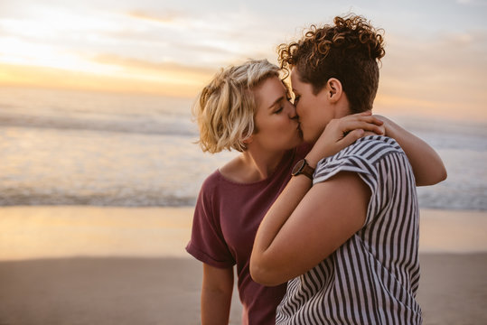 Loving young lesbian couple kissing on a beach at sunset