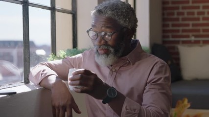 mature african american man drinking coffee at home enjoying relaxed morning looking out window planning ahead thinking successful black businessman smiling wearing glasses - Powered by Adobe