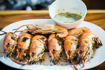 Close up roasted prawn on white plate with spicy sour sauce at seafood market, delicious thai street food 