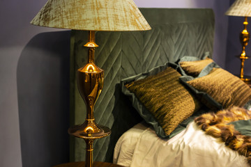 Fragment of beautiful royal bedroom with golden floor lamp and dark green velvet headboard and expensive linens