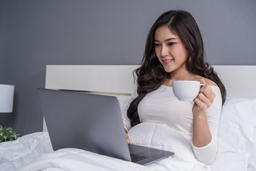 woman drinking a cup of coffee and using laptop computer on bed