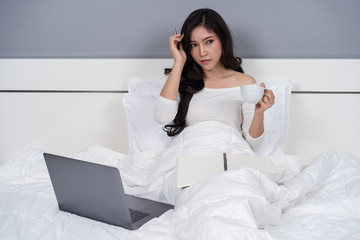 woman thinking and working with laptop computer on bed