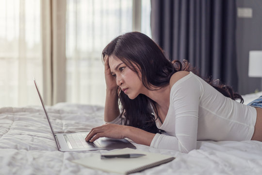 stressed woman using laptop computer on bed