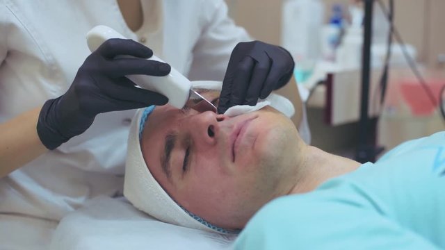 Men`s cosmetology. Young male receiving facial procedures at beauty clinic. Peeling skin