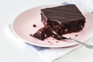 Chocolate vegan brownie cake with nuts. Pink plate. Light background. Selective focus.