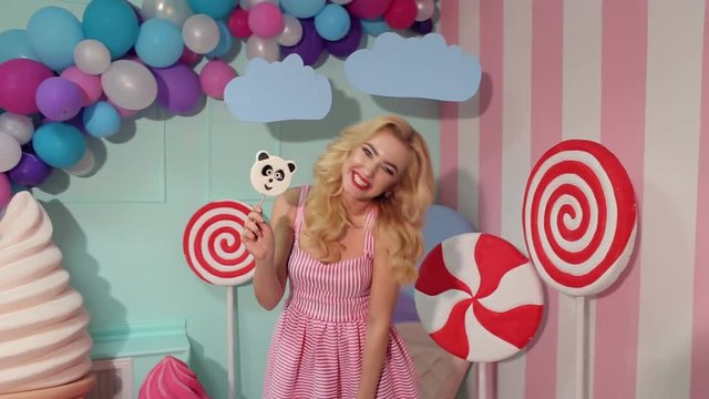Portrait of a Barbie girl with blond curly hair in a pink dress and a big candy in her hands at a candy party. Barbie style.