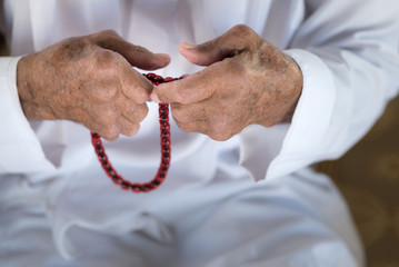 Arabic Bedouin Muslim man  in traditional white holiday clothing.Praying hands of an old man holding rosary beads