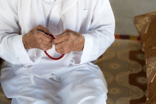 Arabic Bedouin Muslim man  in traditional white holiday clothing.Praying hands of an old man holding rosary beads