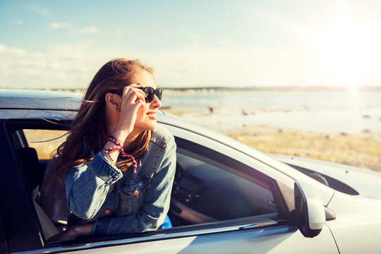 summer vacation, holidays, travel, road trip and people concept - happy smiling teenage girl or young woman in car at seaside