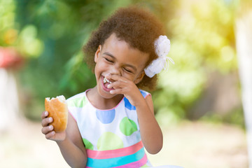 The black girl laughs eating food. A little girl with bread in her hand is having fun on the street.