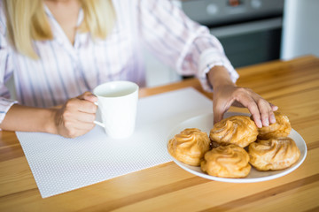 woman in pajamas drinking coffee with pastry in the kitchen