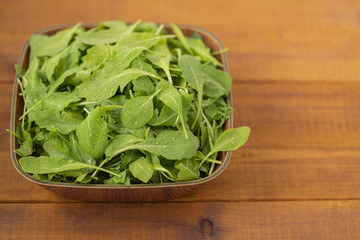Fresh arugula salad in a bowl, on a wooden background.