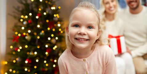family, holidays and people concept - close up of happy little girl with mother and father at home over christmas tree lights background