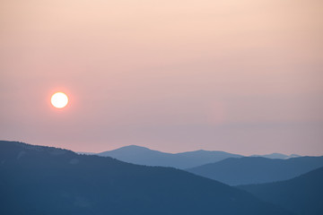 early morning in a mountain, pale sun above a mountain silhouette