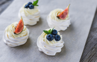 Pavlova meringue cake with figs, blueberries and mint leaves on a wooden background.