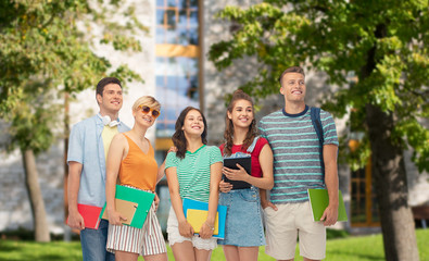 education and people concept - group of smiling students with notebooks, books and folders over campus background