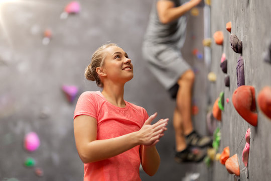 fitness, extreme sport and healthy lifestyle concept - young man and woman bouldering on a rock climbing wall at indoor gym