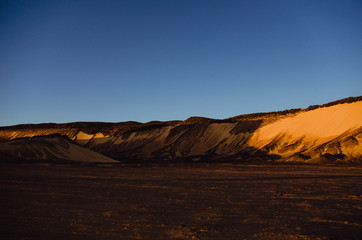 Sunset on the black desert, Black dunes, blue sky