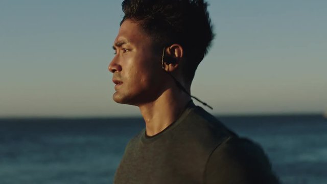attractive young man running athlete runner training tough cardio exercise workout on calm ocean seaside run wearing earphones at sunset close up slow motion