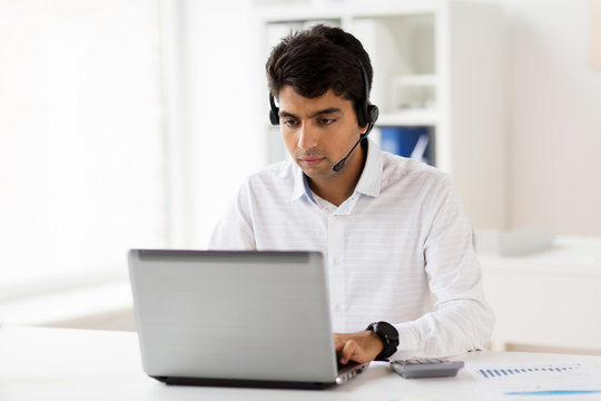 communication, business, people and technology concept - businessman or helpline operator with headset and laptop computer typing at office