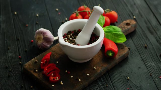 From above view of white mortar and pestle with spices surrounded by pepper and tomatoes on chopping board on wooden background