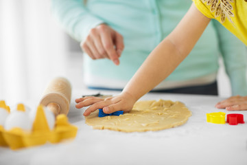 Obraz na płótnie Canvas family, cooking and people concept - mother and little daughter with molds making cookies from dough at home kitchen