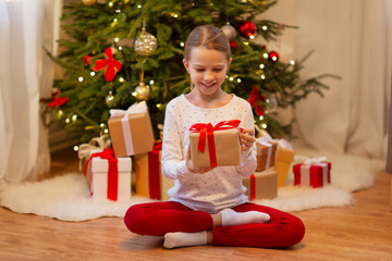 Obraz na płótnie Canvas christmas, holidays and childhood concept - smiling girl with gift box at home