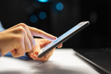 business, deadline and technology concept - close up of businesswoman hands with smartphone at night office