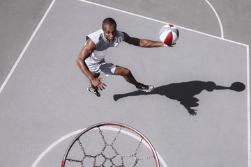 Picture of young confused african basketball player practicing outdoor. Fit afro man in motion and...