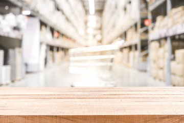Empty wooden table on Blurred of shopping cart boxes on rows of shelves in warm light warehouse background.