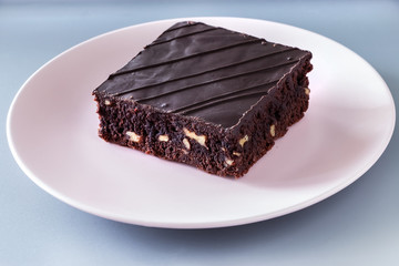 Chocolate vegan brownie cake with nuts pink plate gray background. Selective focus.