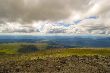 Landscape of green valley flooded with light with lush green grass, mountains, covered with stone and hills, a fresh summer day under a blue sky with white clouds and sun rays in Altai mountains