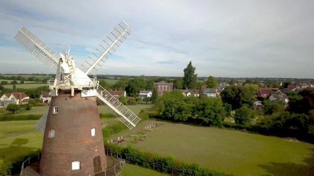 Thaxted Village and Windmill, Essex, England. 4K aerial video footage passing forward through the blades of the old windmill overlooking the rural English village of Thaxted in the Essex countryside.